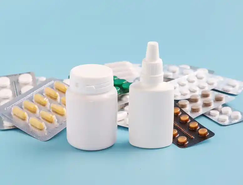 A collection of various medication containers, including a white pill bottle and a spray bottle, surrounded by blister packs of pills on a blue background.