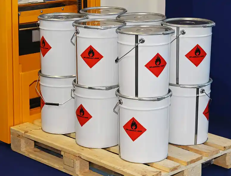 White metal buckets with red hazard labels stacked on a wooden pallet.