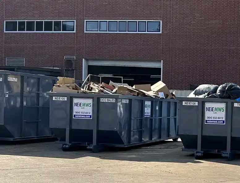 Multiple dumpsters filled with cardboard and other materials, placed in an outdoor area near a brick building.